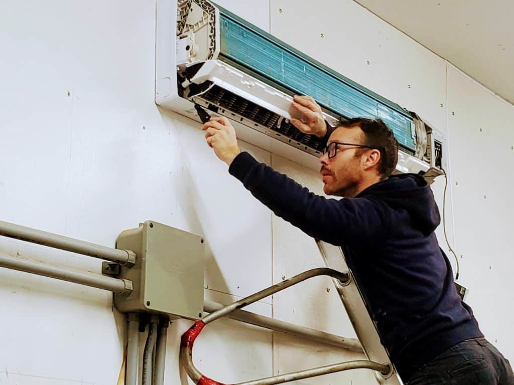 Damian from Pure Air Cleaning removing the front panel of a mini-split heat pump to begin a deep clean