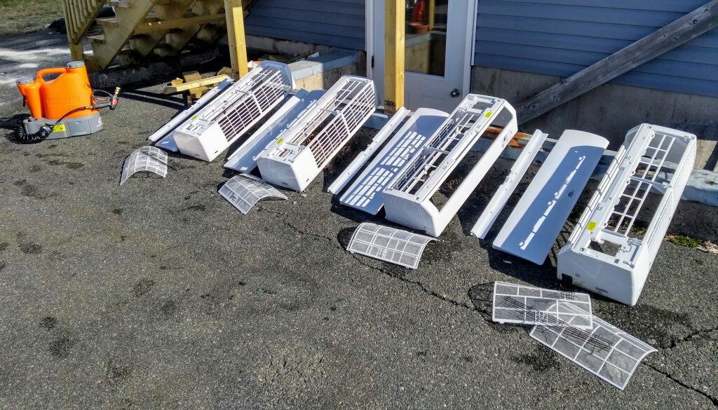 Why a Quick Filter Rinse Won't Clear Deep Heat Pump Mold Washing removable mesh filters and plastic covers during a professional heat pump cleaning service.